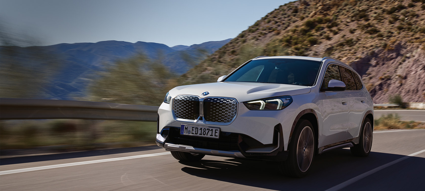 BMW iX1 U11 BEV 2022 Mineral White metallic three quarter front view serpentine mountain road driving